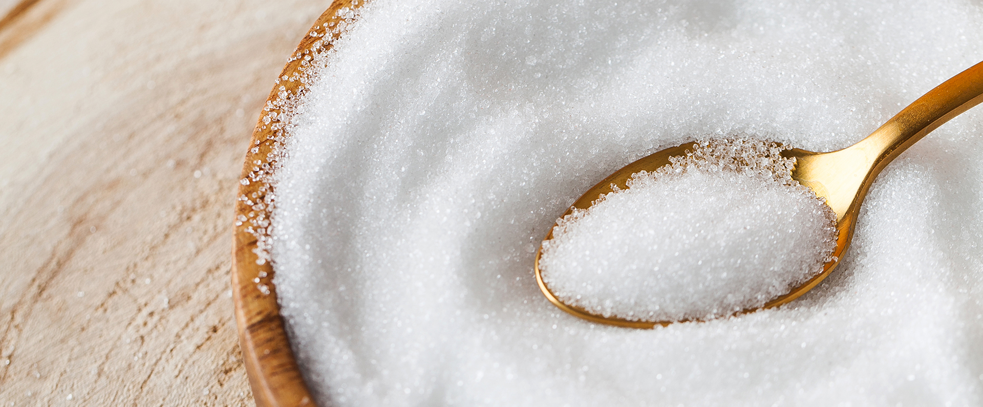 A spoon scooping sugar out of a wooden bowl