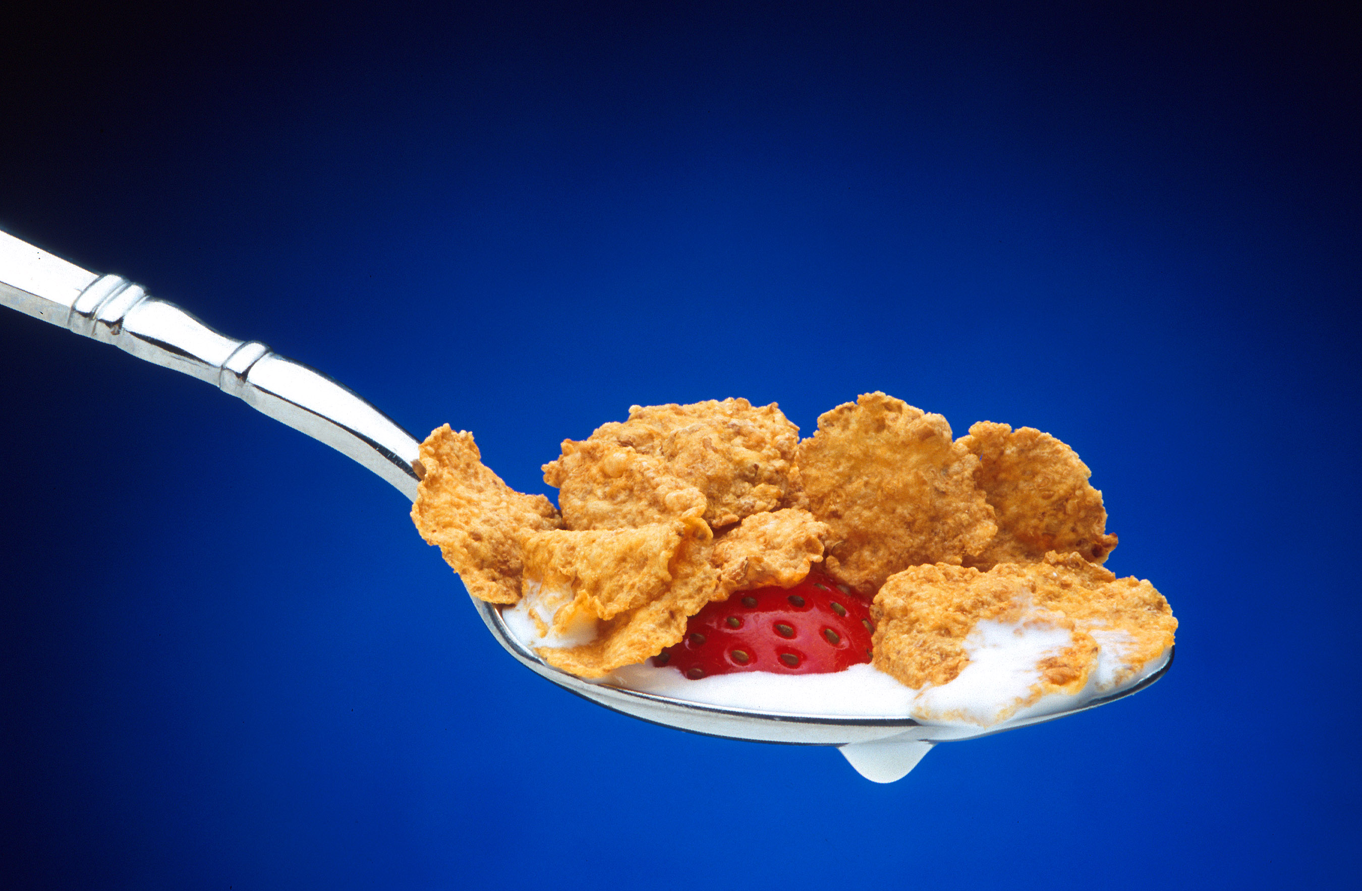 A spoonful of corn flakes, milk and a strawberry