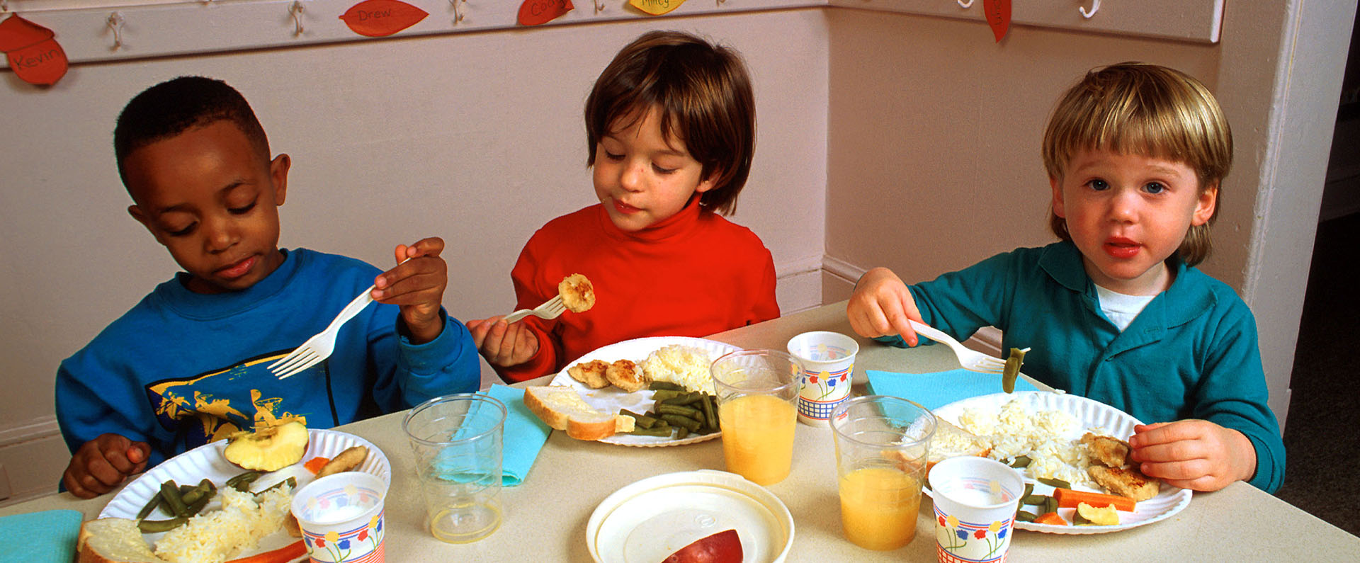 Three young children eating lunch in a classroom