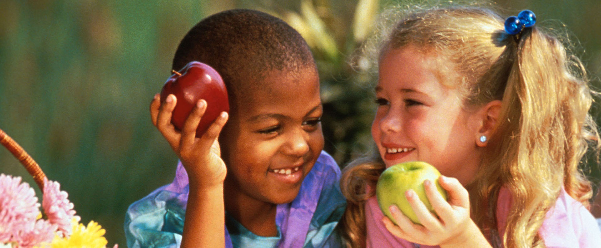 A boy and a girl laying on the ground eating apples. 