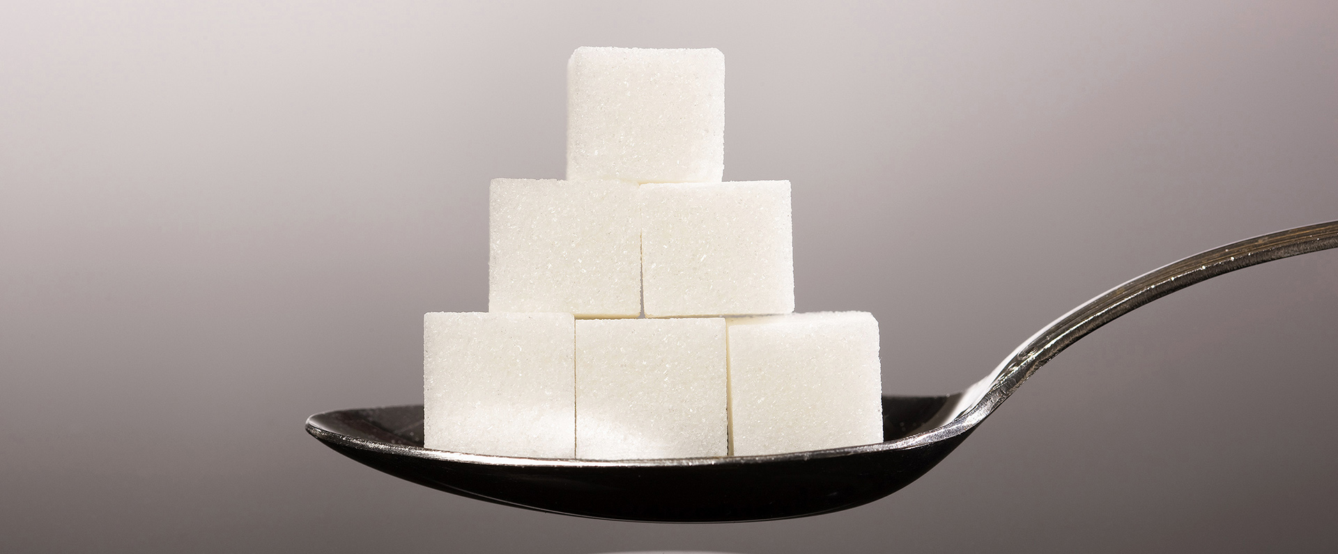 Six sugar cubes stack on a teaspoon.