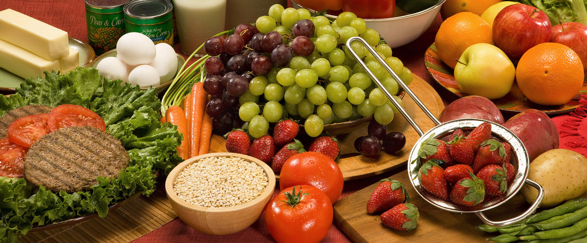 An arrangement of healthy foods including strawberries, grapes, tomatoes, apples, eggs, butter, and oranges. 