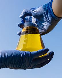 Two gloved hands holding a beaker of biofuel 