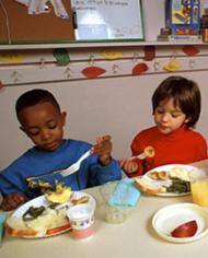 Two preschool children eating lunch in a classroom.